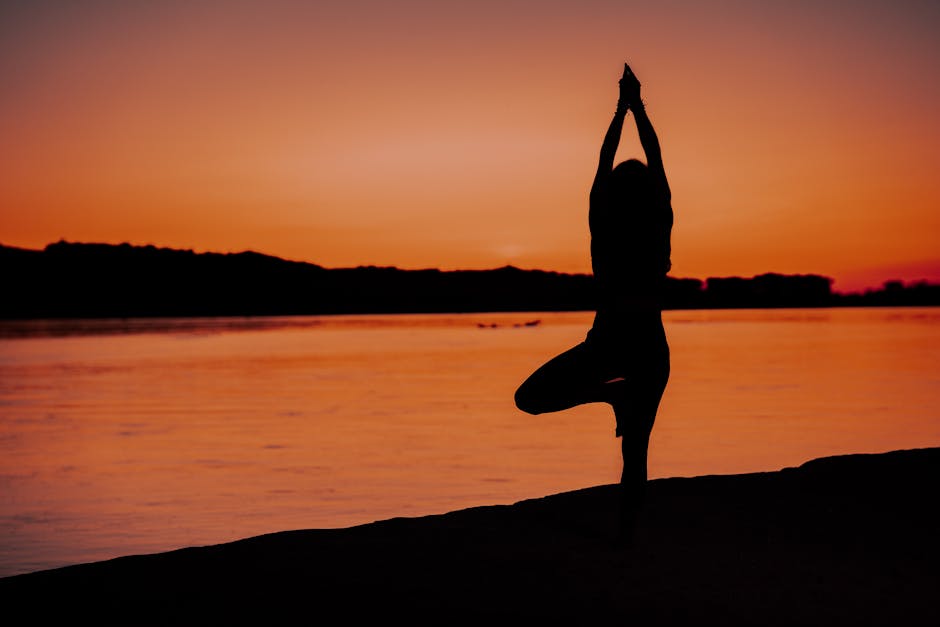 Woman performing a serene yoga pose by a peaceful lake at sunset.